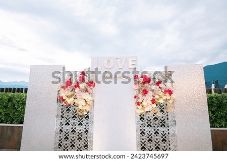 White photo zone stand with colorful bouquets of flowers. Caption: Love forever