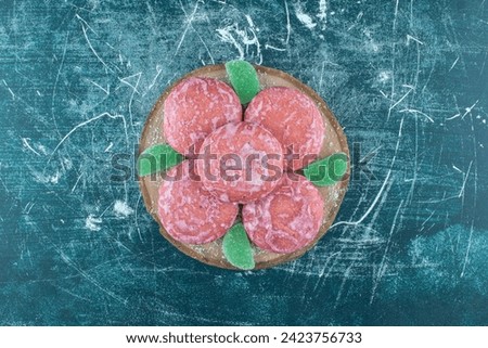 Pink coated cookies and marmelades on a wooden board on blue background. High quality photo