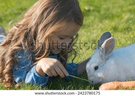 Little girl playing with white rabbit in summer day outdoor
