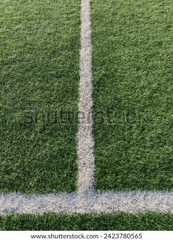This stock photo showcases the central line of a soccer field merging with the crossbar of the sideline, forming an inverted T-shape. The field is made of artificial turf, providing a lush green backd