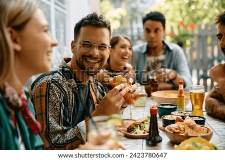 Happy man eating tacos and talking to his friends during their gathering in a restaurant. 