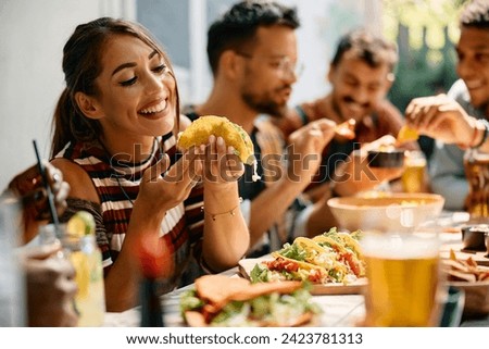 Young woman enjoying in a taste of tacos while having lunch with friends in restaurant.  Royalty-Free Stock Photo #2423781313