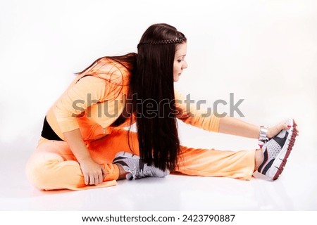 Young Caucasian Woman Sitting On White Background Stretching Out Wearing An Orange Sweat Suit Royalty-Free Stock Photo #2423790887