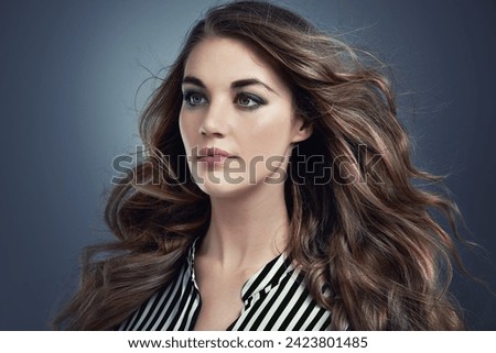 Woman, beauty and hair in studio with cosmetics, thinking of makeup and smokey eye aesthetic. Young and serious model or person with trendy style, treatment and blowing in wind on grey background
