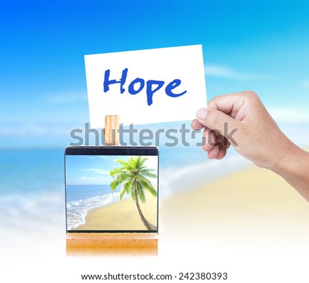 Human hand holding a handwritten HOPE and picture of the beach on paper clip over the actual location.