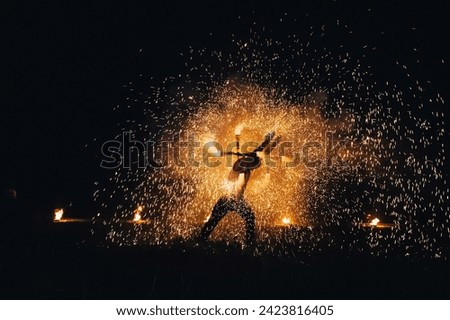 An adult professional man shows a fire show with fire and sparks outdoors at night in the dark in the summer. Photography, entertainment concept. Film effect.