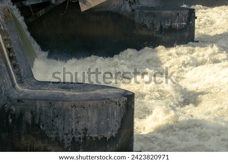 Water shooting through the weir of an electrical power plant, foaming and creating spray. 