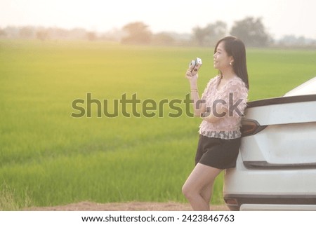 Happy Asian woman taking photo standing near car smiling and relaxing. Travel and transportation concept