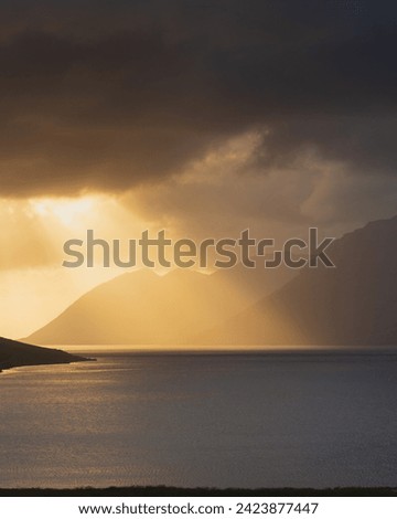 Dramatic sunset over fjord in Westfjords, Iceland. Rays of sunlight shining through dark clouds on water