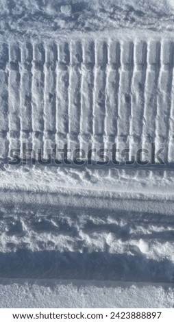 The trail of a snowmobile in the snow, vertical picture of contrast black and white trail on the sparkling snow. Winter road. Background winter landscape.