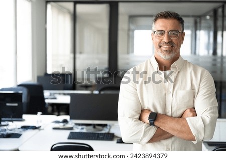 Handsome hispanic senior business man with crossed arms smiling at camera. Indian or latin confident mature good looking middle age leader male businessman on blur office background with copy space.  Royalty-Free Stock Photo #2423894379