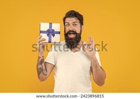 photo of man with present box show ok gesture. man with present box isolated on yellow.