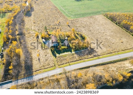 Drone photo of a small farm located in middle of the fields next to the road. Autumn light and colorful trees. Birds eye view of the small household in northern Estonia. Sunny autumn day