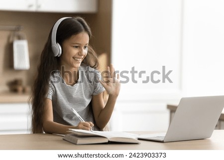 Happy pre teen schoolchild girl using wireless headphones and laptop at home, doing school homework task, talking on video conference call, watching online lesson, attending virtual class