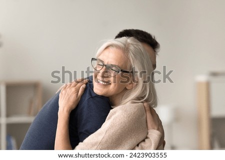Happy affectionate senior mom meeting son at home with greeting hug, embracing adult child with closed eyes, feeling love, tenderness, gratitude. Mature mother casual portrait Royalty-Free Stock Photo #2423903555