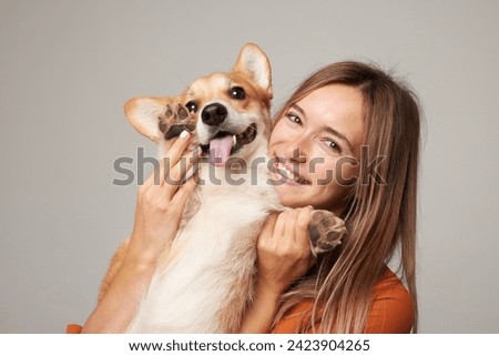 a brunette girl holds and hugs a red corgi dog on a clean light background, the concept of love for animals Royalty-Free Stock Photo #2423904265