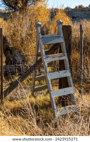 A wooden stile provides individual passage over a  barbed wire fence. Royalty-Free Stock Photo #2423925271