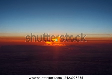 Aerial view of a sunrise with a sunburst effect, featuring a gradient blue sky and clouds lit with fiery orange and red hues, likely taken en route to or from Istanbul. Royalty-Free Stock Photo #2423925755