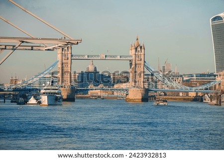 Sunny day at London's Tower Bridge with the River Thames in view, featuring boats and the distant dome of St Paul's Cathedral, highlighting the city's historic architecture.