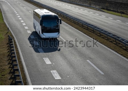 White Modern comfortable tourist bus driving through highway at bright sunny sunset. Travel and coach tourism concept. Trip and journey by vehicle Royalty-Free Stock Photo #2423944317