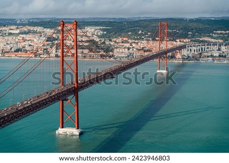 High-angle view of the 25th of April bridge in Lisbon, cloudy sky red steel, over the sea.