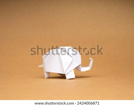 A white elephant paper standing isolated on eco brown kraft paper background. Origami art handcraft style on recycle paper. Elephant care, animals conservation concept.