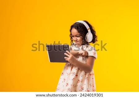 Portrait of angry kid girl with headphones using tablet. Lifestyle, leasure and gadget addiction concept