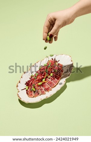 Woman's hand sprinkling green beans over a tuna tataki with vegetable salad, a representation of a healthy concept. Royalty-Free Stock Photo #2424021949