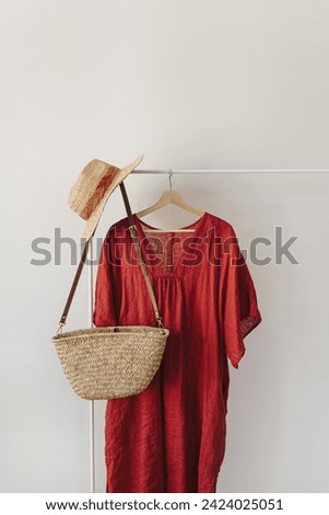 Straw hat, straw handbag, red dress on clothes rack over white wall