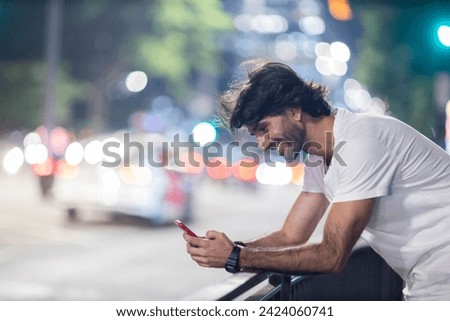 View of young man using a smartphone at night time with city view landscape in the background. High quality photo. 