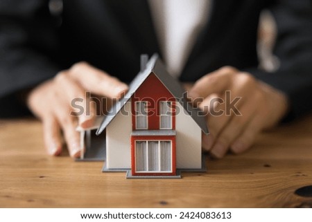 Hands of real estate, insurance agent touching toy house on work table, promoting rent of apartment. Female realtor, mortgage broker offering loan for property buying. Close up cropped shot