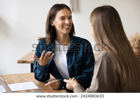 Cheerful young female managers talking at office workplace table, discussing creative ideas for startup project, enjoying teamwork, collaboration, success, laughing, having fun Royalty-Free Stock Photo #2424083633