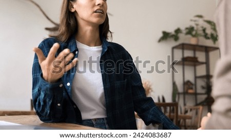 Serious young professional woman in informal clothes talking to colleague at work desk, moving hand, explaining startup project strategy, discussing collaboration. Cropped banner shot Royalty-Free Stock Photo #2424083687