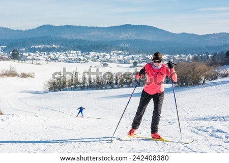 Woman cross country skiing. Ascending a slope with another skier following.
