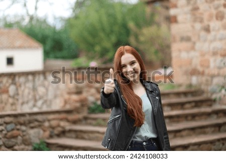 Pretty girl on the street smiles satisfied with raised finger Royalty-Free Stock Photo #2424108033
