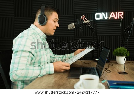 Hispanic man with headphones recording a podcast episode or hosting a radio talk show in the studio reading a script