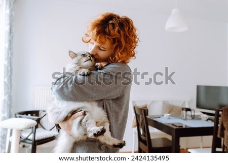 funny red-haired teenage girl holds pet in arms, hugs and kisses purring Maine Coon cat. Friendship between pet and its owner, Cat Moms Royalty-Free Stock Photo #2424135495