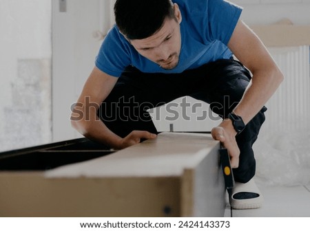 A young man is repairing an old wardrobe. Royalty-Free Stock Photo #2424143373