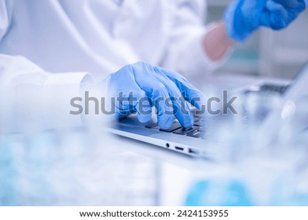 Closeup woman female scientist's hand blue protective glove using laptop for recording scientific medical experiment research from laboratory