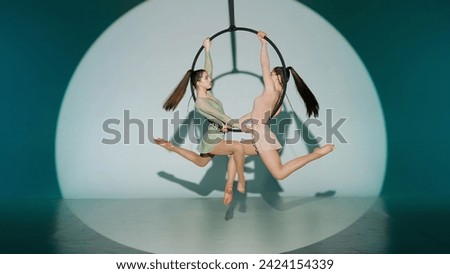 Two female gymnasts isolated on green studio background. Girls aerial dancers showing mirrored element on ring with straps.