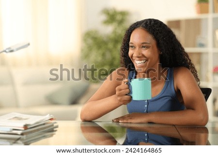 Happy black woman drinking coffee and laughing at home Royalty-Free Stock Photo #2424164865