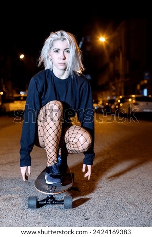 Young woman in shorts on a long board while looking camera at night in the city