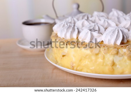Tasty homemade meringue cake and cup of tea on wooden table, on light background