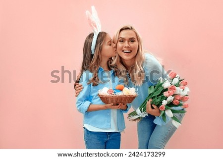 We are ready for the celebration! Cute lovely nice sweet mommy and small daughter holding basket with colored eggs and a bouquet of tulips isolated on pink background.