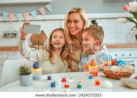 Happy Easter! Charming mother with her children cute boy and girl take a selfie while they paint eggs. Happy family getting ready for Easter.