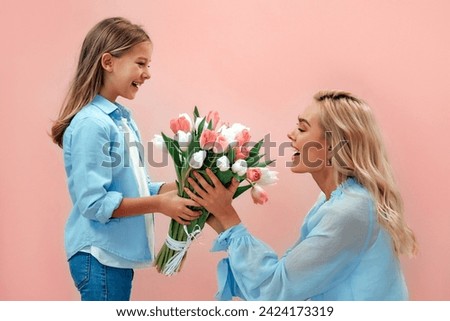 Happy Mother's Day! Cute charming girl gives her beautiful mother a bouquet of tulip flowers isolated on pink background. Royalty-Free Stock Photo #2424173319