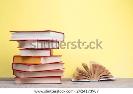 Composition with hardback books, fanned pages on wooden deck table and yellow background. Books stacking. Back to school. Copy Space. Education background. Tuition payment.
