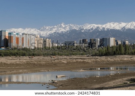 Storage reservoir Lake Sayran, Almaty, Kazakhstan. Empty City sand beach with drained pond. Residential apartment buildings and high snow-capped mountains in background. Recreation place for citizens Royalty-Free Stock Photo #2424174831
