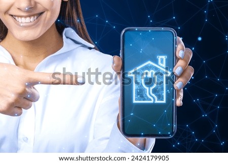 Happy smiling businesswoman pointing at smartphone with smart home icon on blue polygonal background. Technology and innovation concept