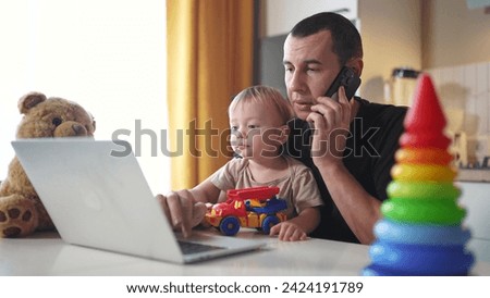 father working from home remotely with baby son in his arms. pandemic remote work business concept. father tries to work at home in kitchen, baby children interfere sitting on their fun hands Royalty-Free Stock Photo #2424191789